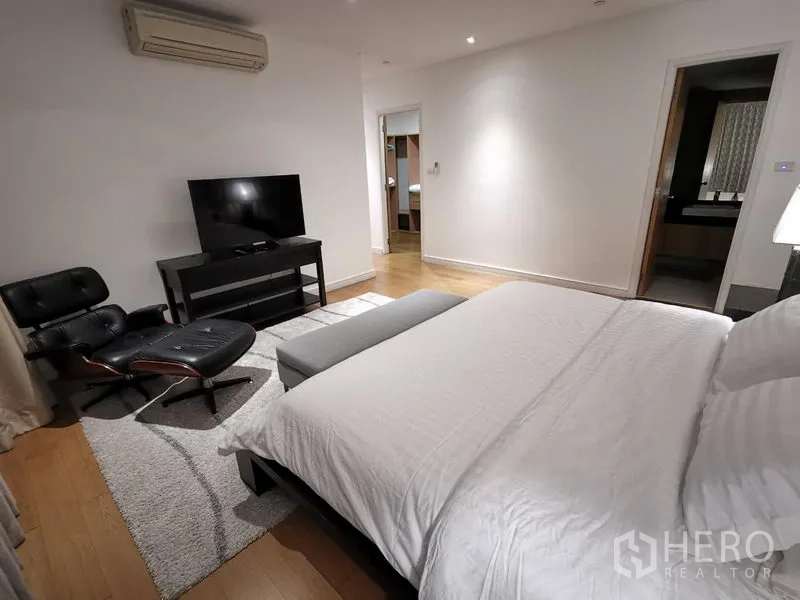 Condominium for rent in Watthana, Bangkok - Primary bedroom angle showing TV console, ensuite access, and an Eames-style lounge chair.