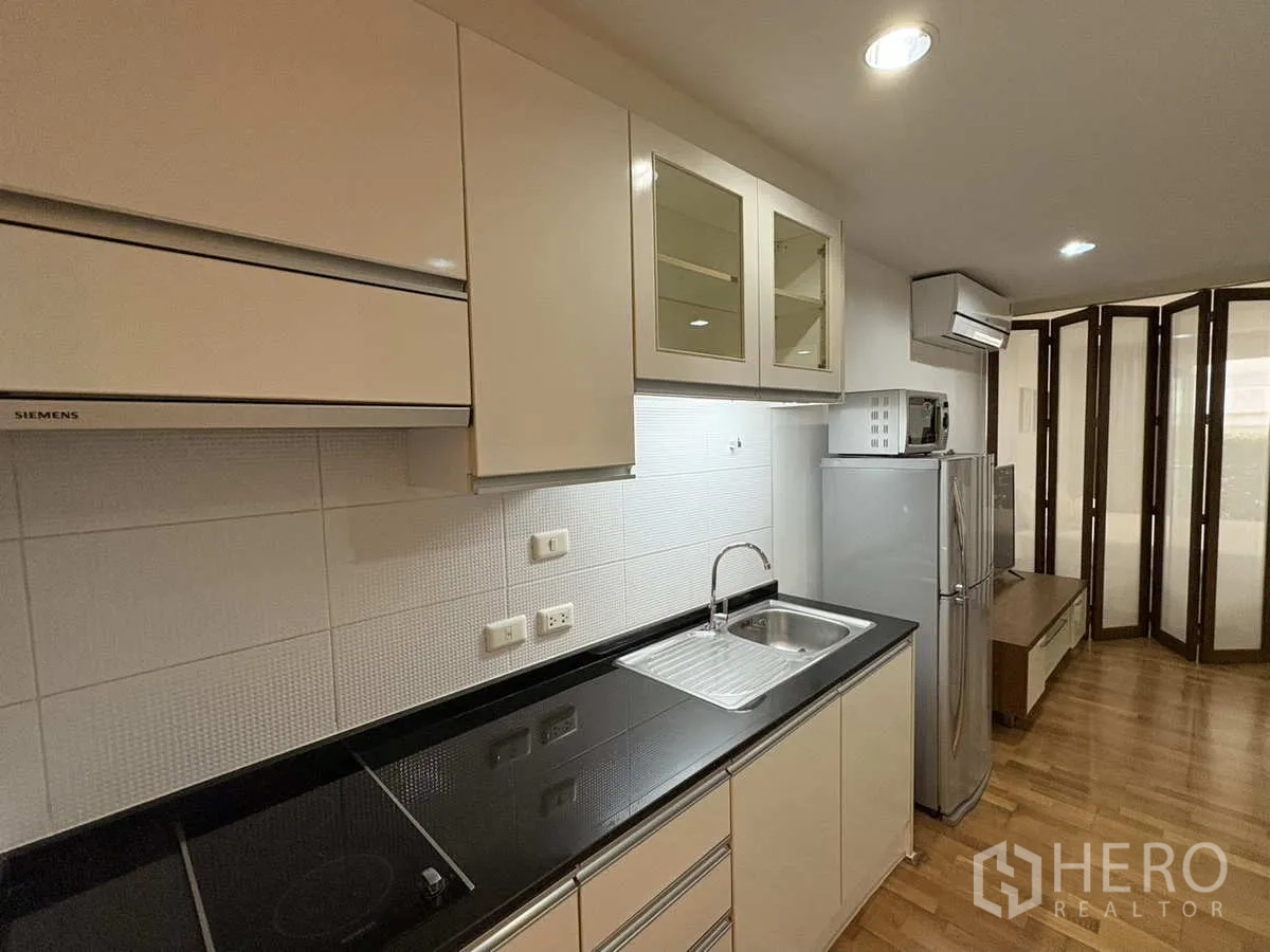 公寓 出租在Khlong Toei, Bangkok - 整体厨房配亮面柜体、电磁炉、水槽与黑色台面。