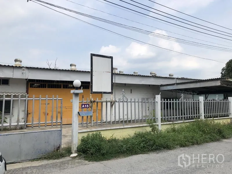 Warehouse for rent in Sai Mai, Bangkok - Street-facing warehouse exterior with security fence, sign frame, and a yellow main gate.
