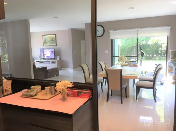Detached House for rent or sale in Prawet, Bangkok - View from the kitchen to the dining area with a six-seat table and wide windows to greenery.