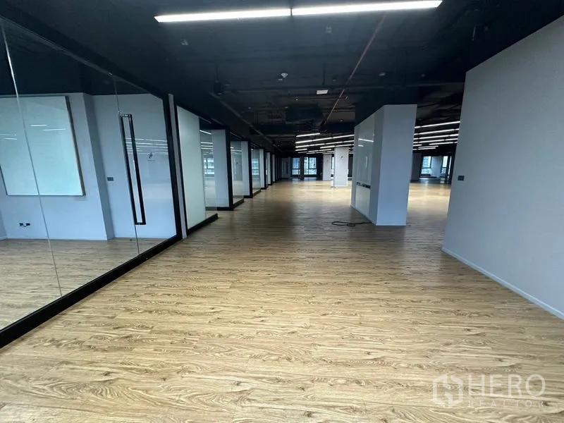 Office Space for rent in Bang Rak, Bangkok - Wide corridor through office with glass partitions, mirrors, and wood flooring.