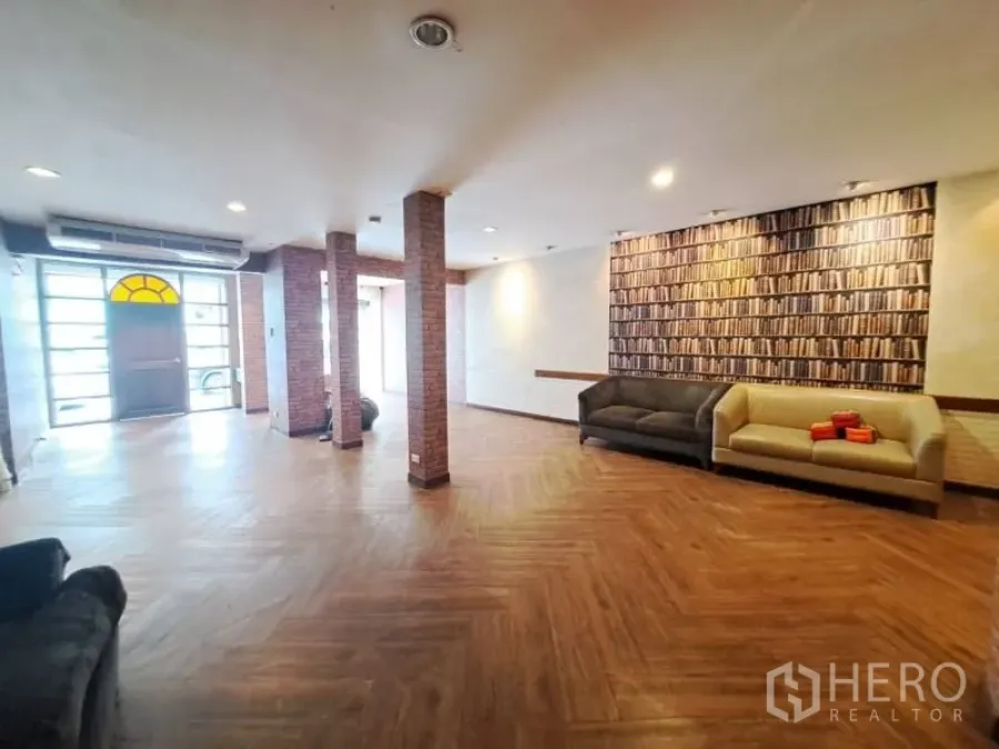 店屋 出租在Watthana, Bangkok - 宽敞大厅，鱼骨木地板、裸露砖柱与沙发。