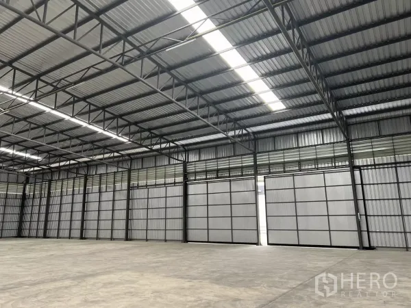 Warehouse for rent in Lat Lum Kaeo, Pathum Thani - Interior view with multiple sliding loading doors, steel beams, and skylights providing natural light.