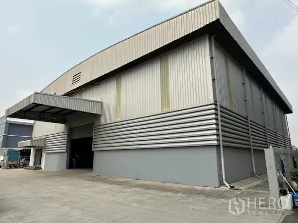 货栈 出租在Bang Phli, Samut Prakan - 金属板外墙仓库转角视角，带覆盖装卸口与卡车通道。