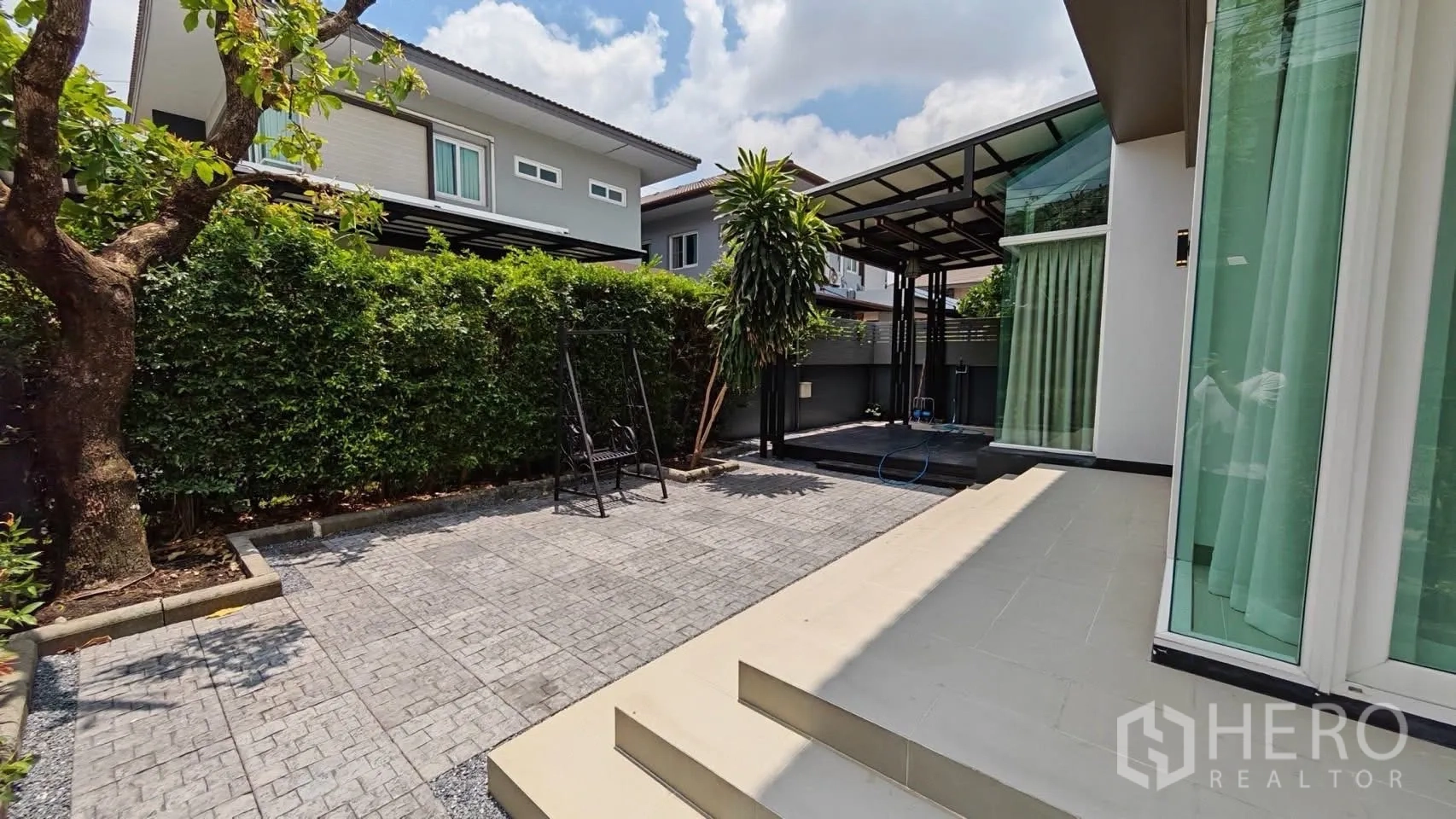 Detached House for rent or sale in Bang Phli, Samut Prakan - Paved yard with privacy hedges, a swing seat, and a raised wooden deck.