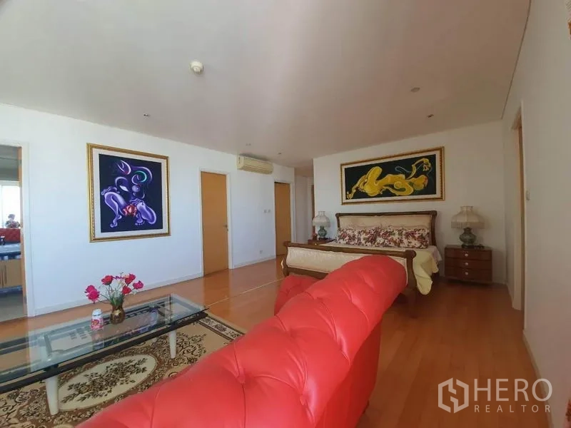 คอนโด ขายในWatthana, Bangkok - ห้องนอนกว้างพร้อมโซฟาหนังสีแดง โต๊ะกระจก งานศิลป์ติดผนัง และพื้นไม้โทนอบอุ่น