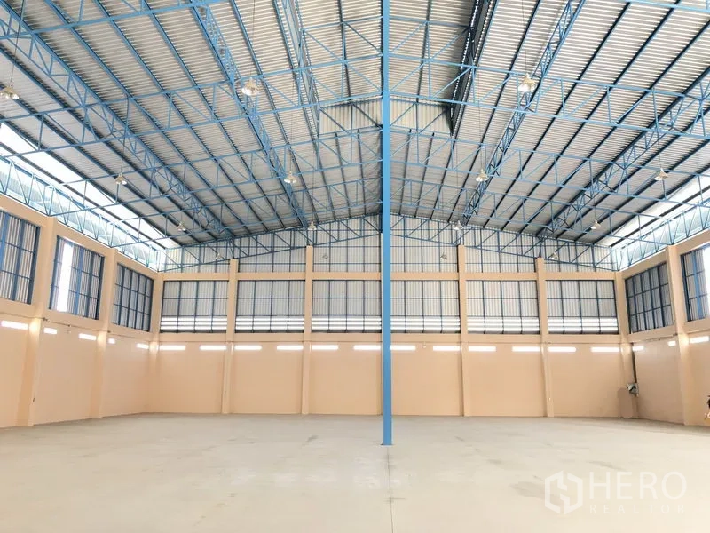 Warehouse for rent in Lat Lum Kaeo, Pathum Thani - Expansive warehouse interior with high 11–16 m ceiling and blue steel trusses.