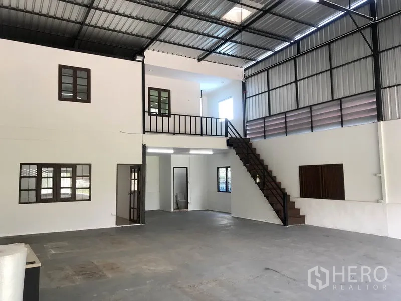 Warehouse for rent in Lam Luk Ka, Pathum Thani - Spacious warehouse interior with high steel roof, mezzanine office, staircase, and concrete floor.
