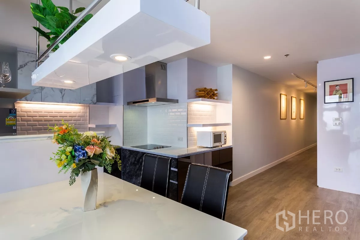 Condominium for rent or sale in Watthana, Bangkok - Bright kitchen with a marble breakfast bar, induction cooktop and a lit hallway.