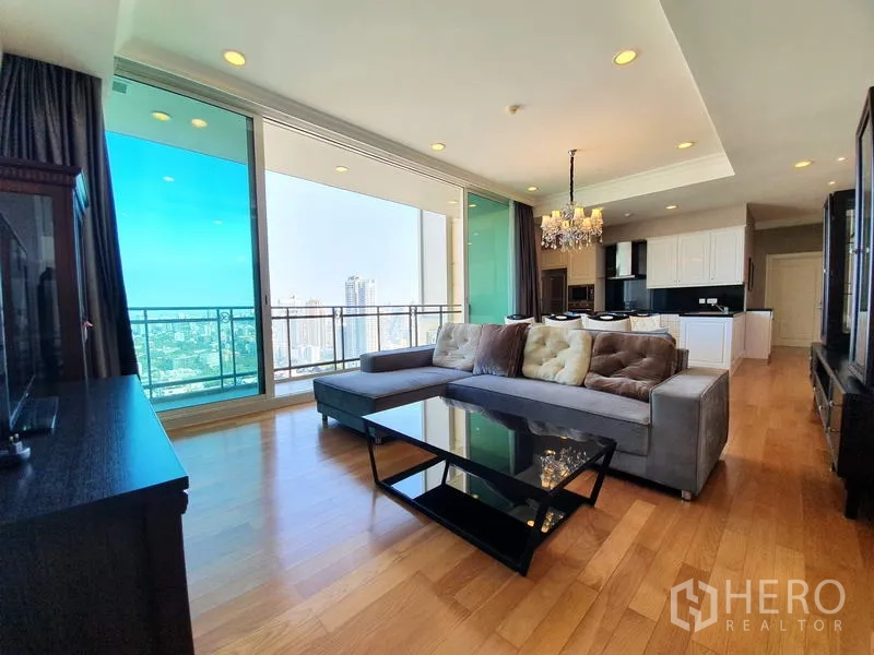 公寓 出租在Watthana, Bangkok - 宽敞客厅，木地板、转角沙发与阳台框景曼谷天际线。