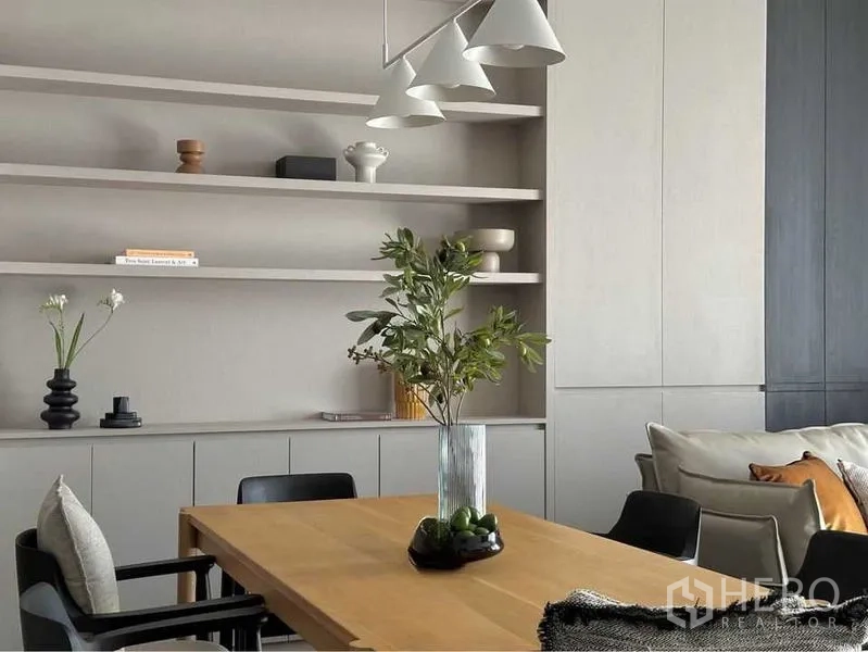 Condominium for rent or sale in Watthana, Bangkok - Dining area with wooden table, open shelving and contemporary pendant lighting beside sofa.