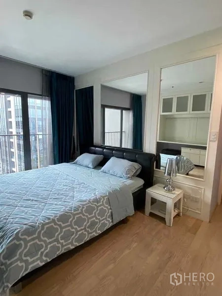 Condominium for rent in Khlong Toei, Bangkok - Corner bedroom with floor-to-ceiling windows, blue drapes and bedside table.
