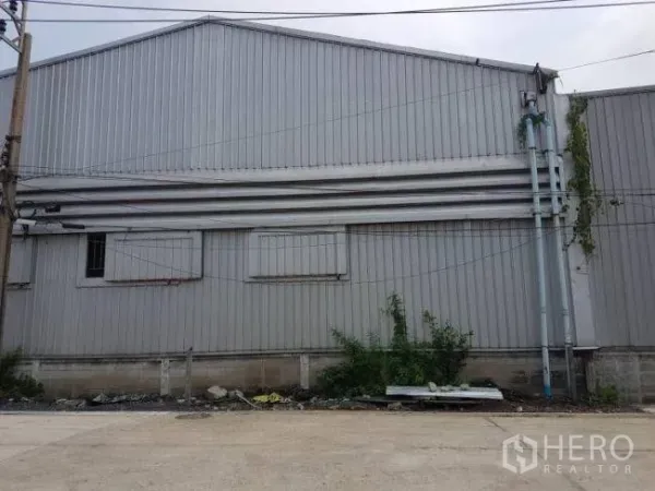 Factory for rent or sale in Bang Phli, Samut Prakan - Street view of a grey corrugated-metal factory wall with vents and utility pipes in Bang Phli.