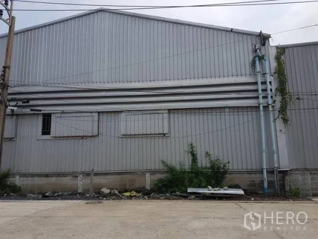 Factory for rent or sale in Bang Phli, Samut Prakan - Street view of a grey corrugated-metal factory wall with vents and utility pipes in Bang Phli.