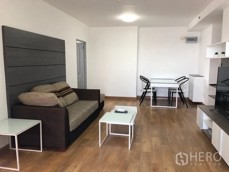 Condominium for rent in Huai Khwang, Bangkok - Spacious living and dining room with sofa, coffee table, and dining set on warm wood flooring.