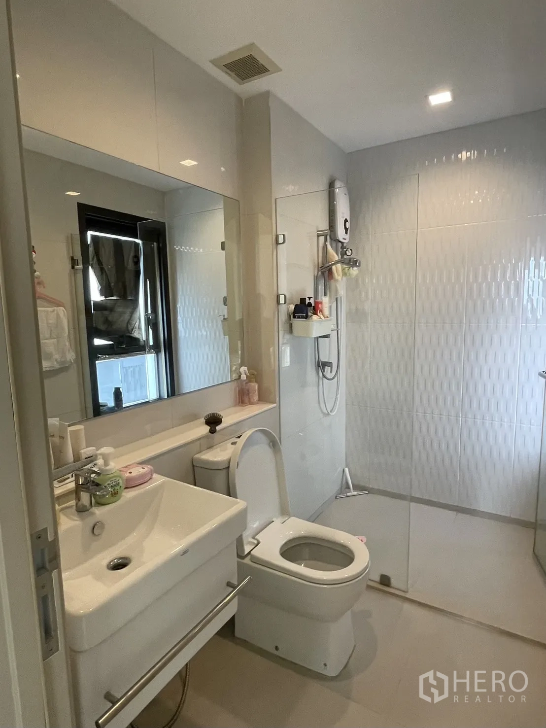 Condominium for rent in Pathum Wan, Bangkok - Modern bathroom with large mirror, white vanity, toilet and a glass-enclosed walk-in shower.