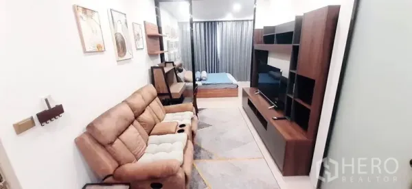Condominium for rent or sale in Huai Khwang, Bangkok - Living room and TV unit leading to a glass-partitioned bedroom.