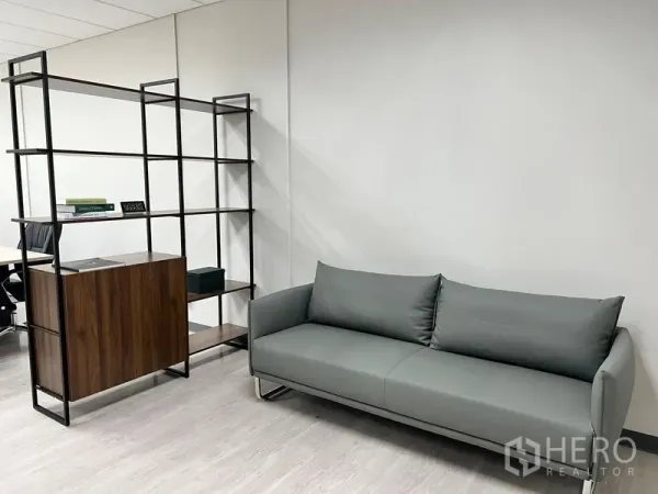 Office Space for rent in Sathon, Bangkok - Reception corner featuring a gray sofa and open metal-wood shelving on light wood flooring.