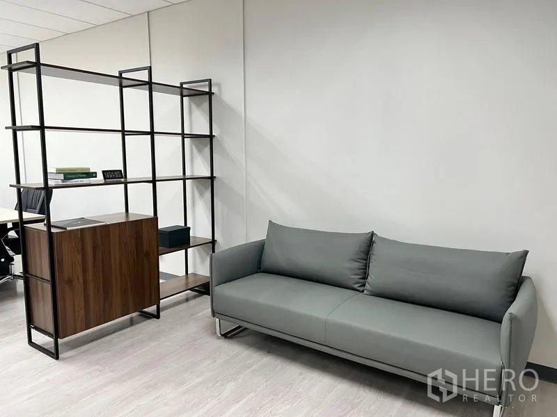 Office Space for rent in Sathon, Bangkok - Reception corner featuring a gray sofa and open metal-wood shelving on light wood flooring.