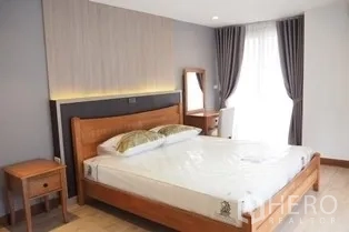 Condominium for rent in Pathum Wan, Bangkok - Bedroom with wooden bed, vanity desk and floor-to-ceiling window curtains.