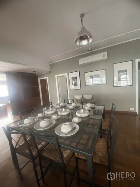 公寓 出租在Sathon, Bangkok - 餐厅另一角度，装饰画、壁挂空调与玻璃餐桌藤椅。