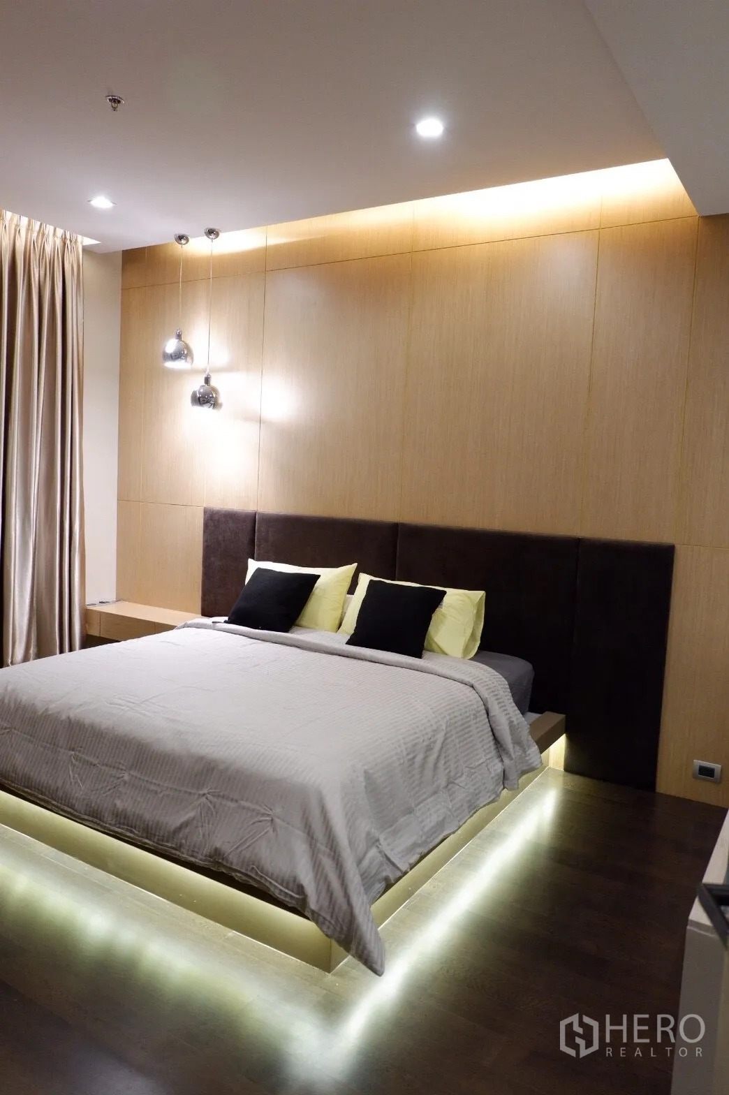 公寓 出租在Watthana, Bangkok - 主卧配平台床及床下LED氛围灯，木质墙面，吊灯与深色木地板。