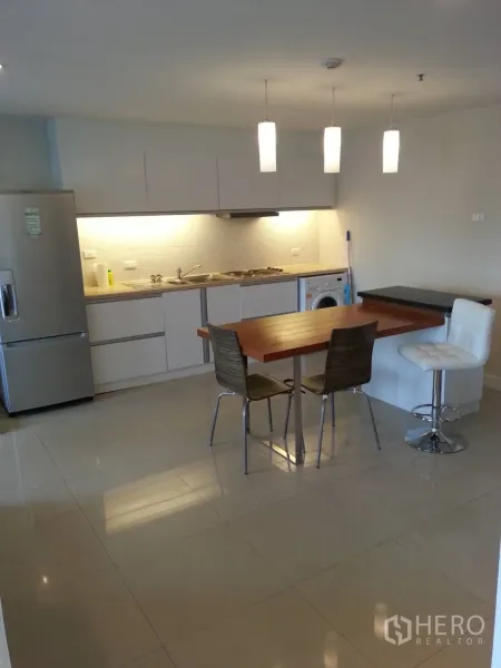 Condominium for rent in Ratchathewi, Bangkok - Open-plan kitchen with white cabinetry, pendant lights, dining table and washer.