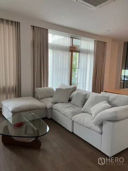 独立式住宅 出租在Saphan Sung, Bangkok - 采光充足的客厅，白色转角沙发、落地窗与玻璃茶几，木地板。