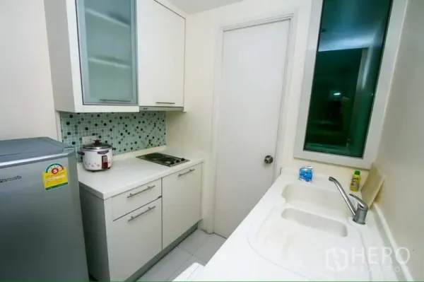 公寓 出租在Ratchathewi, Bangkok - 紧凑的一字型厨房，马赛克墙面、白色橱柜、双槽水槽与侧门。