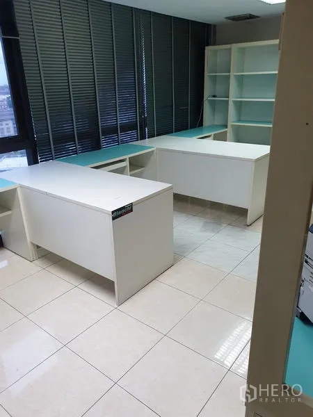 Office Space for rent - Workroom with two white desks, shelving and city-view windows.