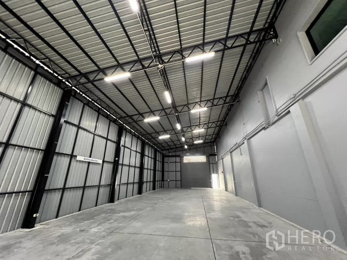 货栈 出租在Yan Nawa, Bangkok - 狭长仓库通道，金属夹层墙体，尽头为卷帘门出入口。