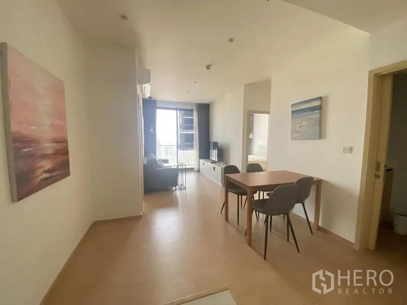 Condominium for rent in Watthana, Bangkok - Open‑plan dining and lounge with four‑seat table, light wood floors, and large sliding doors to a balcony.