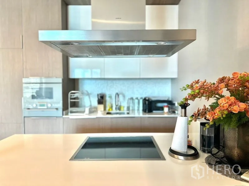 Condominium for rent in Pathum Wan, Bangkok - Kitchen island cooktop with stainless hood and flowers on the counter.