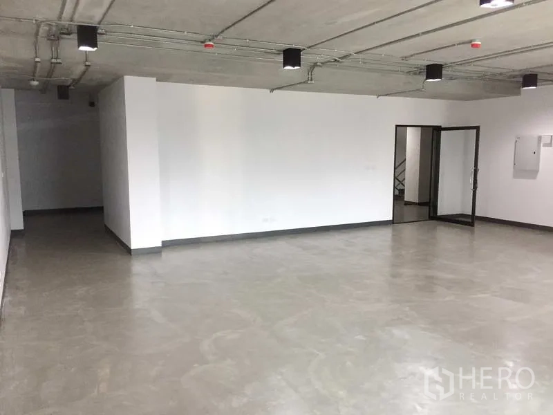 Office Space for rent in Khlong Toei, Bangkok - Open-plan 87 sqm office with polished concrete floors, white walls, exposed ceiling lights, and a glass entry door.