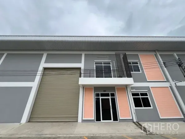 工厂 出租在Phra Samut Chedi, Samut Prakan - 面街工厂外观，超高卷闸门与两层办公室玻璃入口。