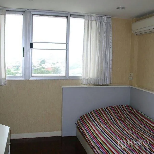 Condominium for rent in Watthana, Bangkok - Corner bedroom with striped bedding, large windows, air conditioner and city view.
