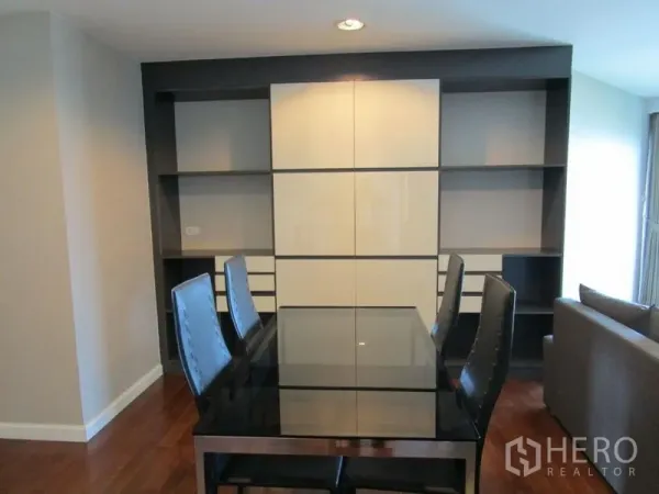 Condominium for sale in Huai Khwang, Bangkok - Dining space with glass table, high-back chairs, and built-in shelving wall