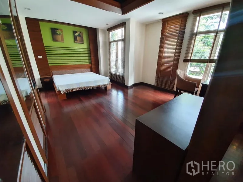 Detached House for rent in Wang Thonglang, Bangkok - Spacious master bedroom with wood floors, large windows and a green feature wall behind the bed.