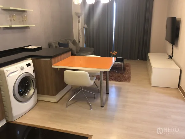 คอนโด ให้เช่าหรือขายในKhlong Toei, Bangkok - พื้นที่นั่งเล่นและทานอาหาร โต๊ะสีส้ม โซฟา ทีวีติดผนัง และผ้าม่านเต็มสูง