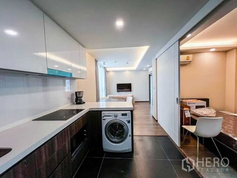 Condominium for sale in Huai Khwang, Bangkok - View from the kitchen toward the living area with peninsula counter, washer and a sliding door to a second room.