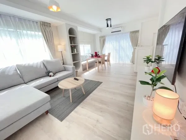 联排别墅 出租在Prawet, Bangkok - 宽敞客厅与餐区，内置展示架、落地窗帘，采光充足。