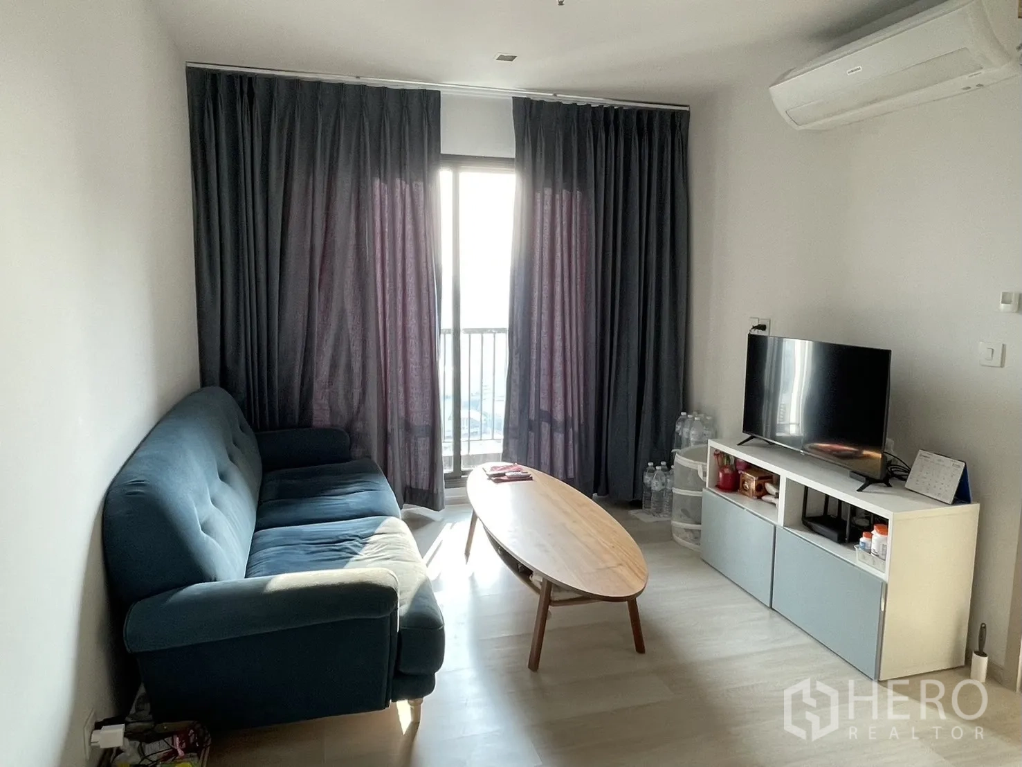 公寓 for rent in Pathum Wan, Bangkok - 客厅设蓝色沙发、电视柜，并可通往阳台，配高窗帘。