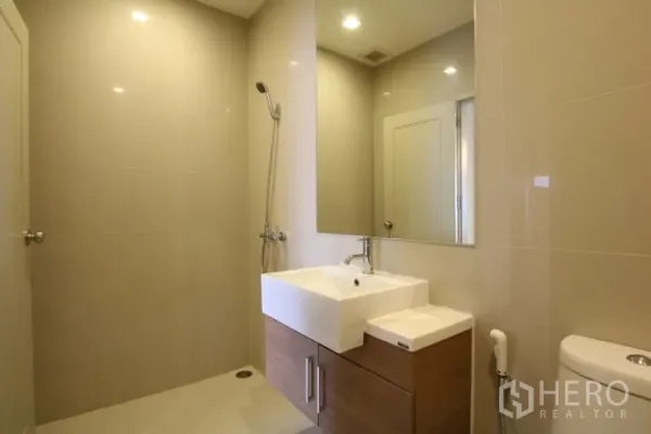 Condominium for rent or sale in Watthana, Bangkok - Modern bathroom with walk-in shower, large mirror, vanity cabinet and neutral tiles.