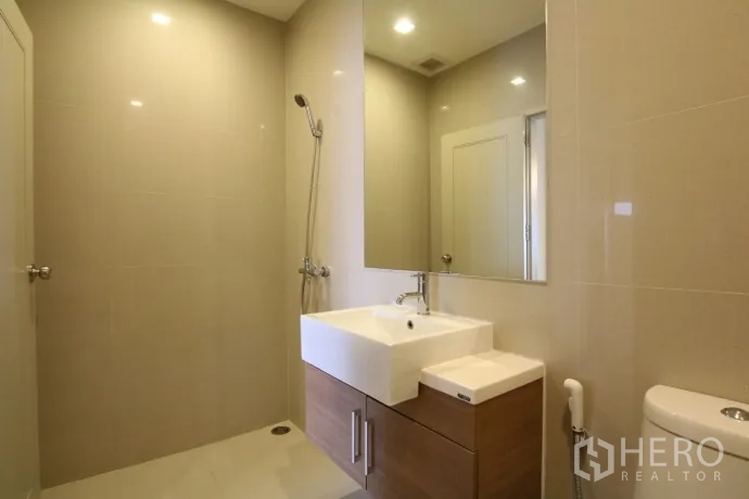 Condominium for rent or sale in Watthana, Bangkok - Modern bathroom with walk-in shower, large mirror, vanity cabinet and neutral tiles.