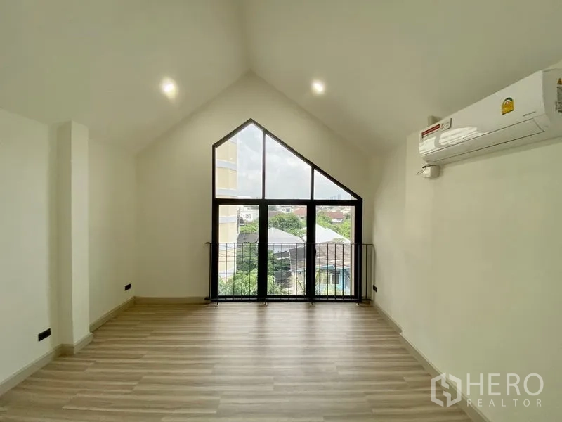 Home Office for rent or sale in Bang Na, Bangkok - Top-floor room with vaulted ceiling and a large triangular window overlooking greenery.