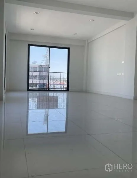 Home Office for rent or sale in Suan Luang, Bangkok - Spacious white-tiled room with recessed lighting and a sliding glass door opening to a small balcony and city view.