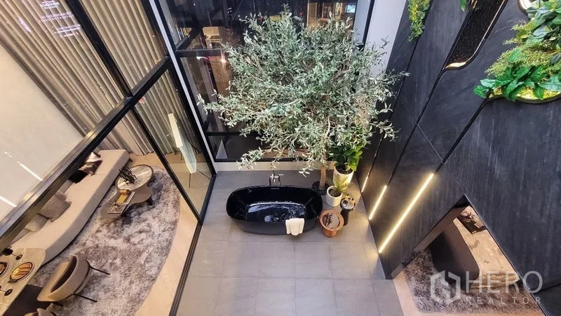 Detached House for sale in Watthana, Bangkok - Top view of an indoor tree and black tub beside floor-to-ceiling windows and gray tiled floor.