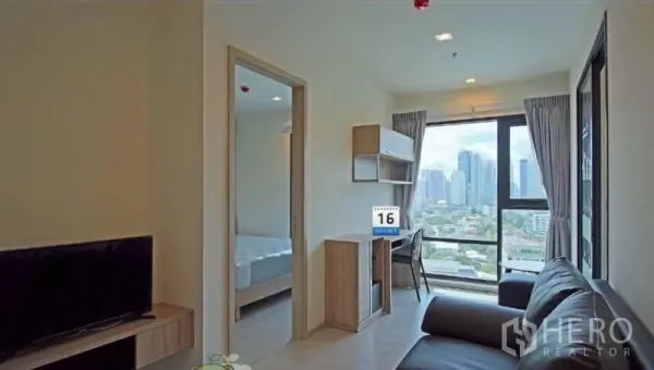 Condominium for rent in Khlong Toei, Bangkok - Living room with TV console and study nook overlooking a panoramic city skyline.
