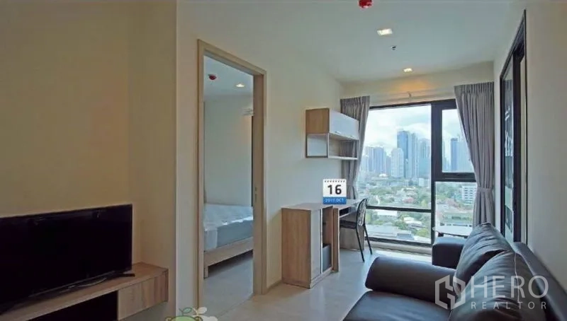 Condominium for rent in Khlong Toei, Bangkok - Living room with TV console and study nook overlooking a panoramic city skyline.
