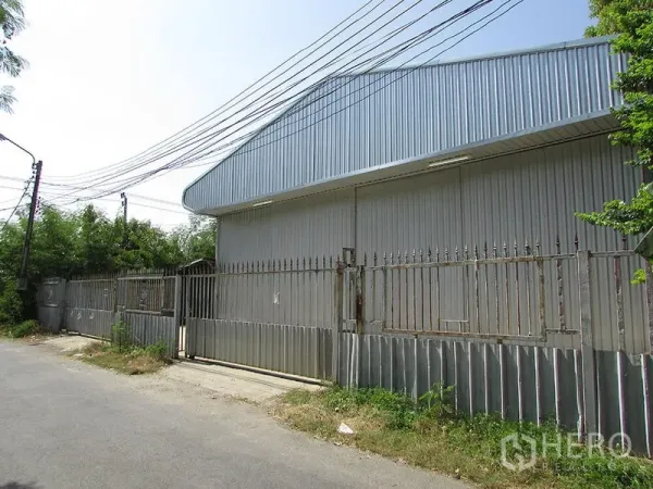 货栈 出租在Bang Khen, Bangkok - 邦肯安静小路旁的镀锌金属仓库外观，带围栏与大型滑动门。